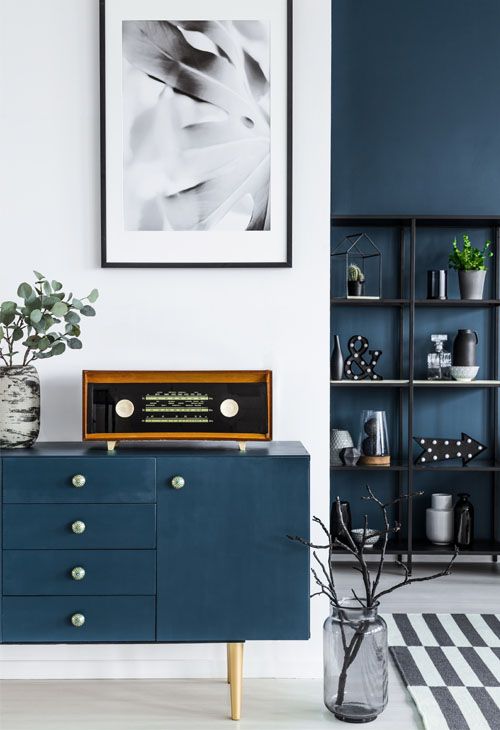 Close-up of a painting, blue cabinet, retro radio and glass vase with branches in dark living room interior and metal shelf in the background.