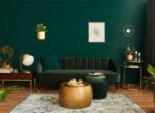 Luxury living room in house with modern interior design, green velvet sofa, coffee table, pouf, gold decoration, plant, commode, carpet, and elegant accessories.